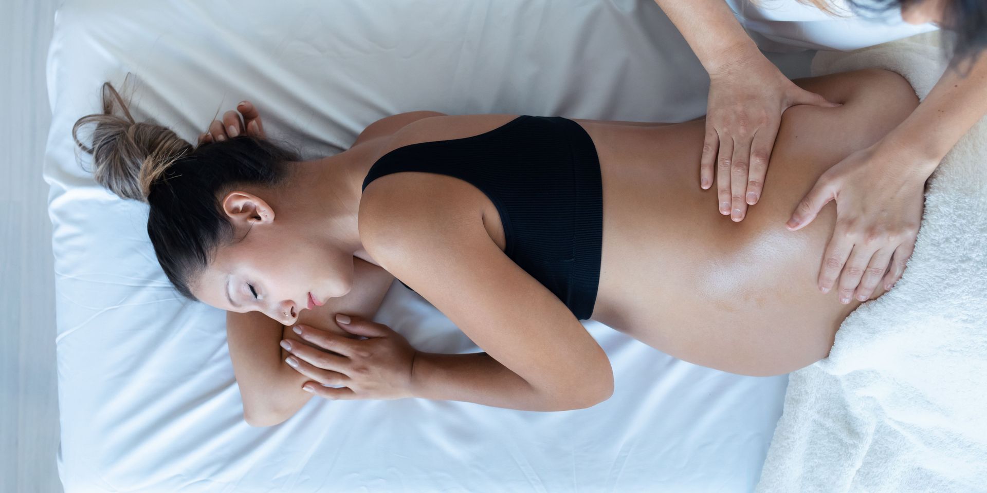 A pregnant woman is laying on a bed getting a massage.