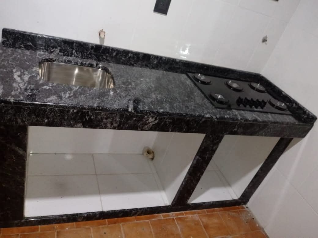 Encimera de cocina con fregadero y estufa; granito negro, base de baldosas blancas, piso beige.