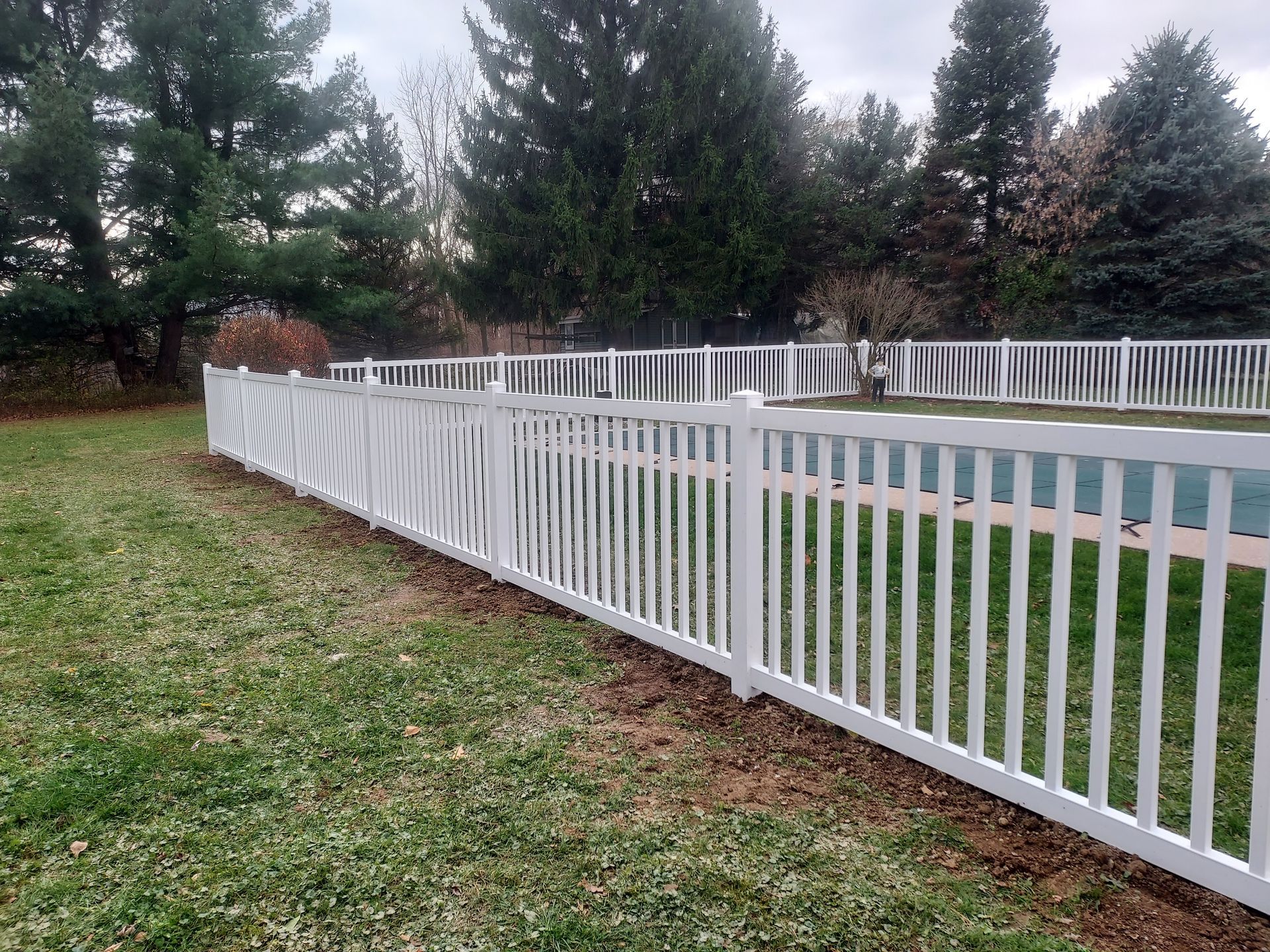 A white fence surrounds a swimming pool in a backyard.