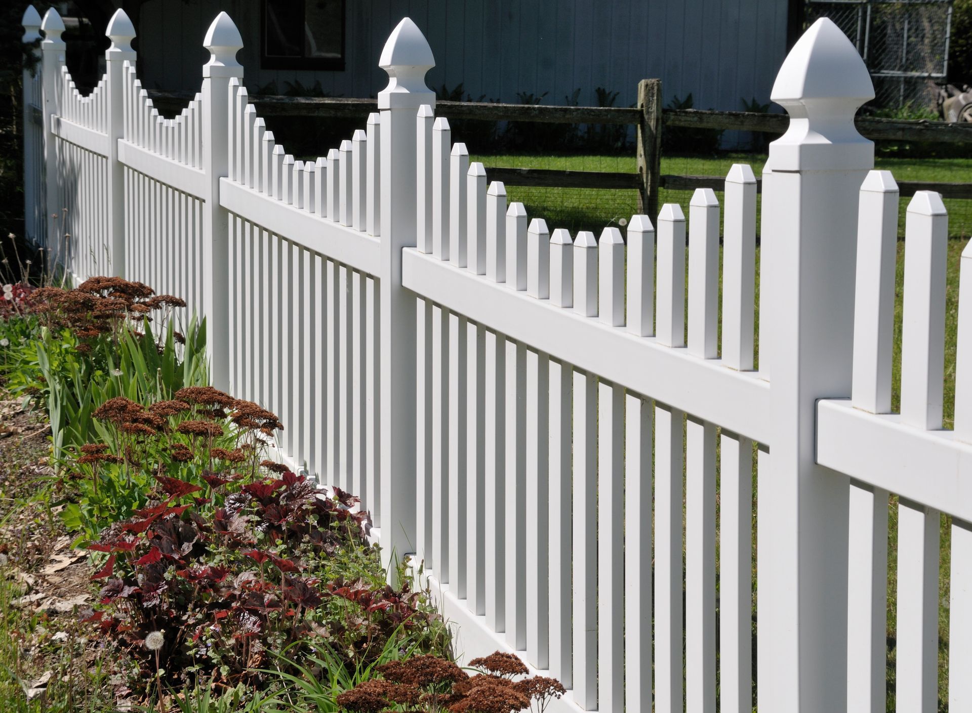 A white picket fence surrounds a garden in front of a house