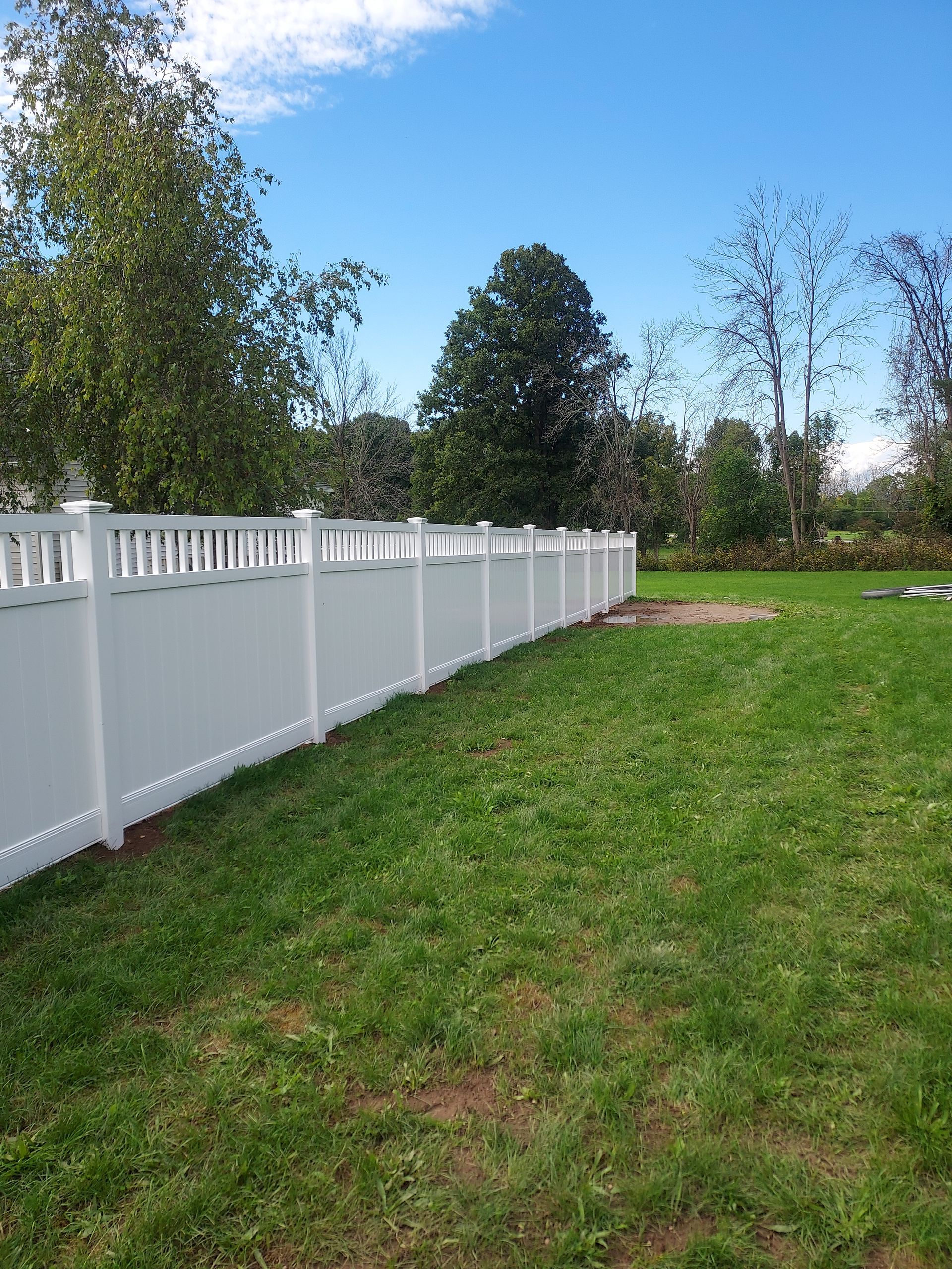 A white vinyl fence surrounds a lush green field.