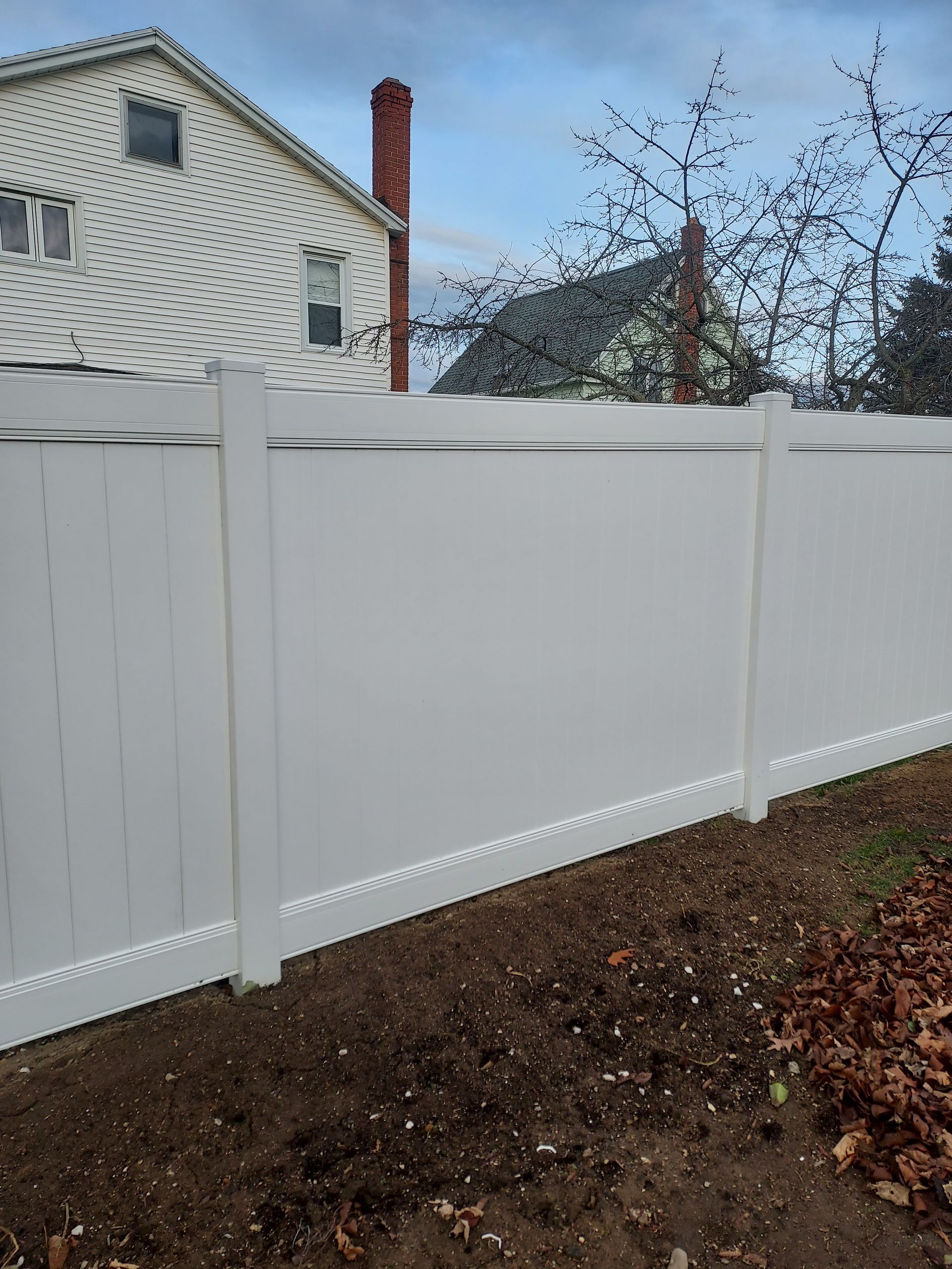 A white fence is sitting in the dirt in front of a house.