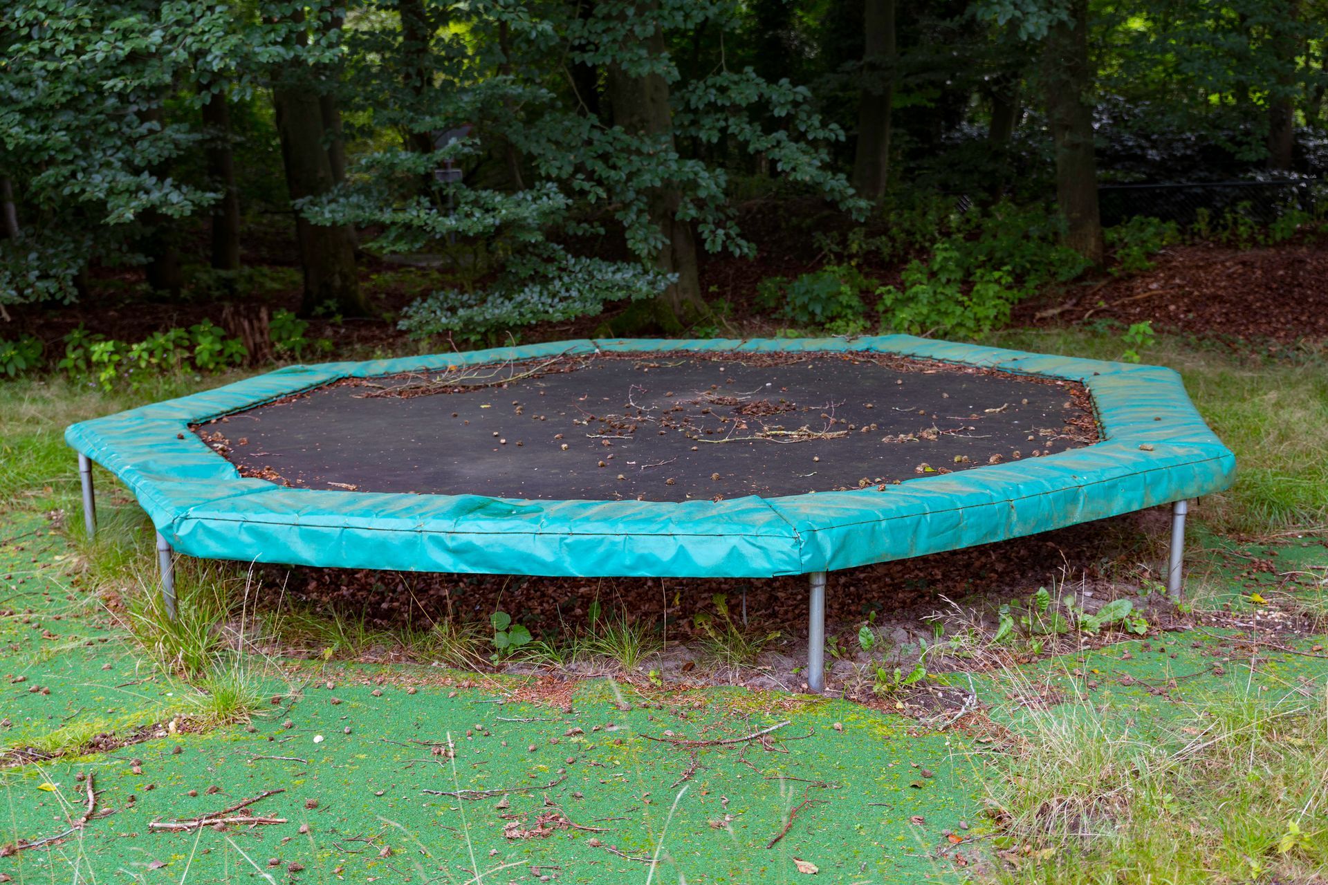 An empty trampoline is sitting in the middle of a lush green field.