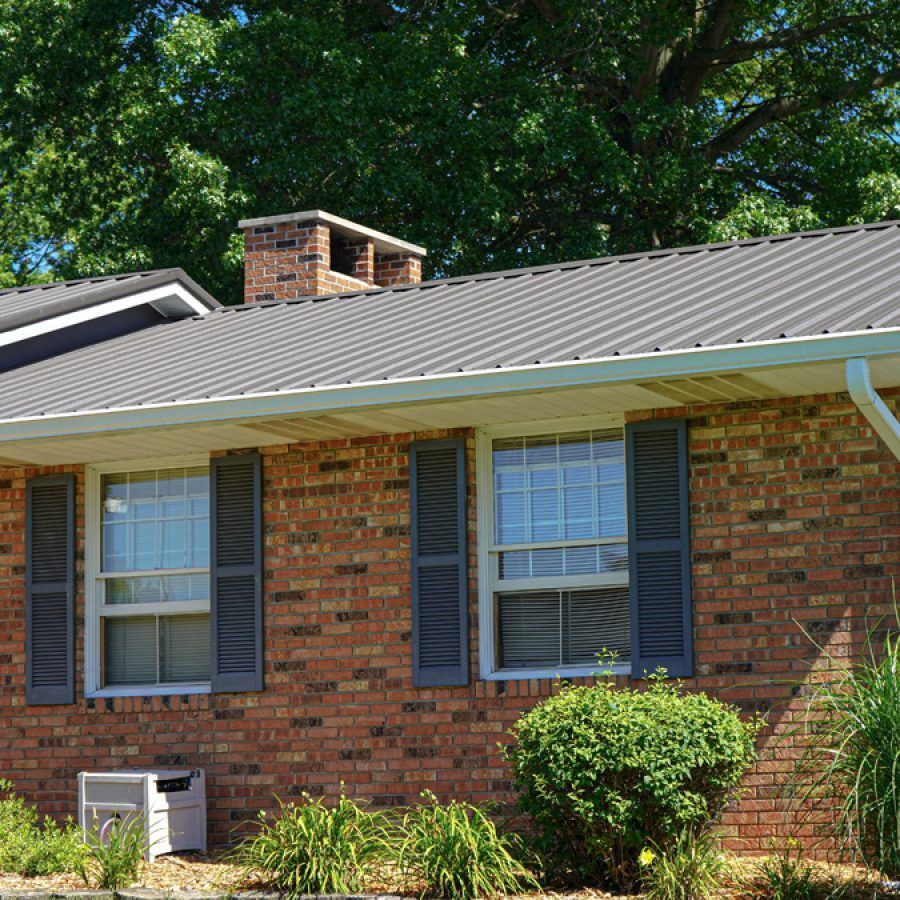 Brick house with a dark gray metal roof, white trim, and blue shutters replacement