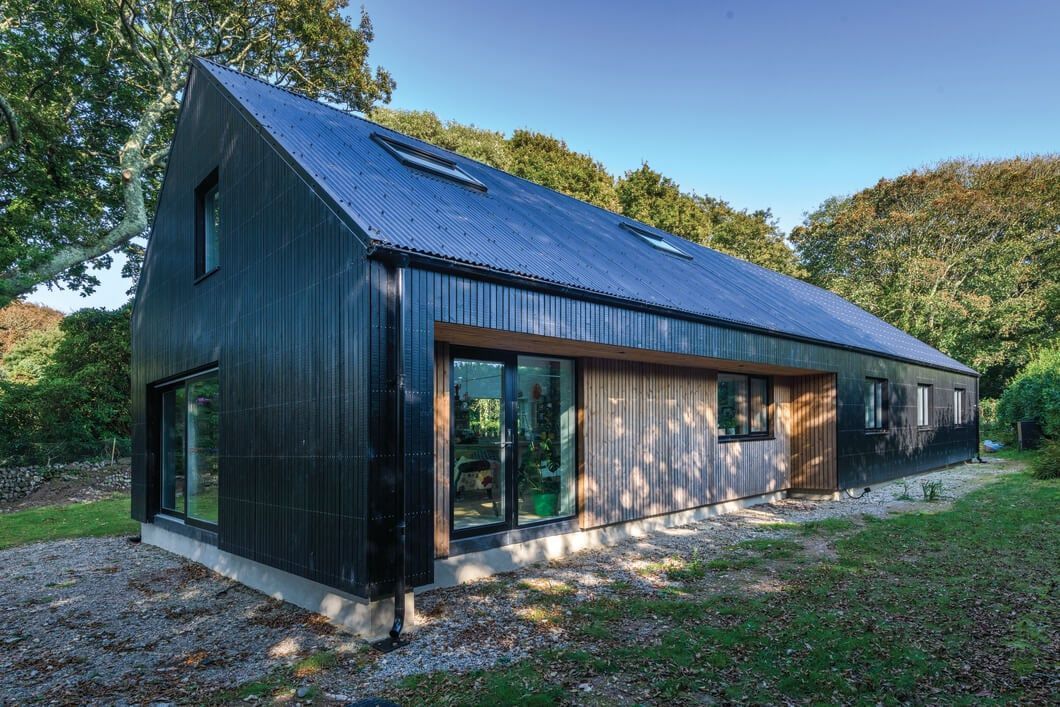 Modern, black-clad house with a corrugated metal roof and wood paneling. New construction.