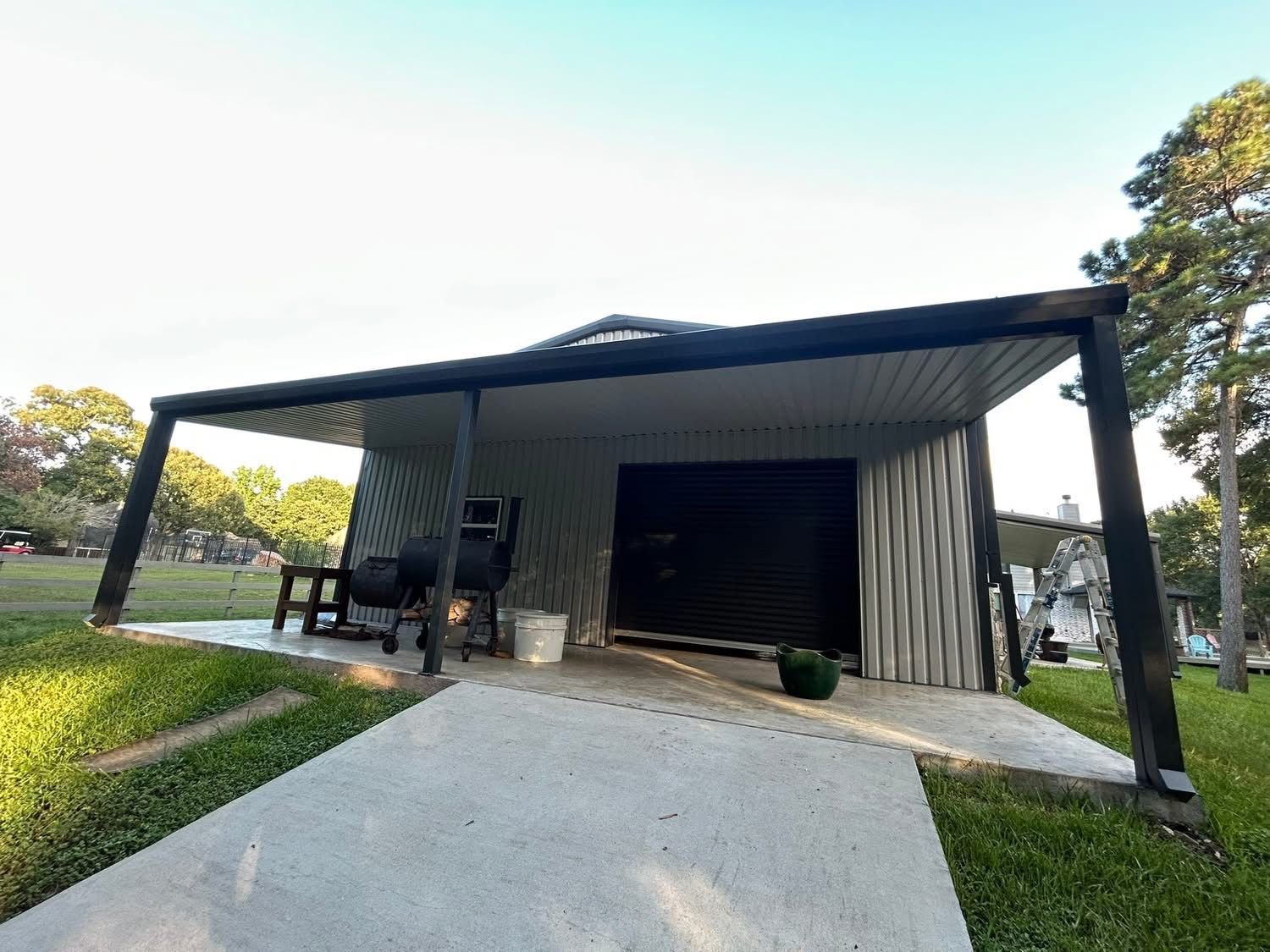 A new metal building shed with a black roof and supports, with a concrete patio
