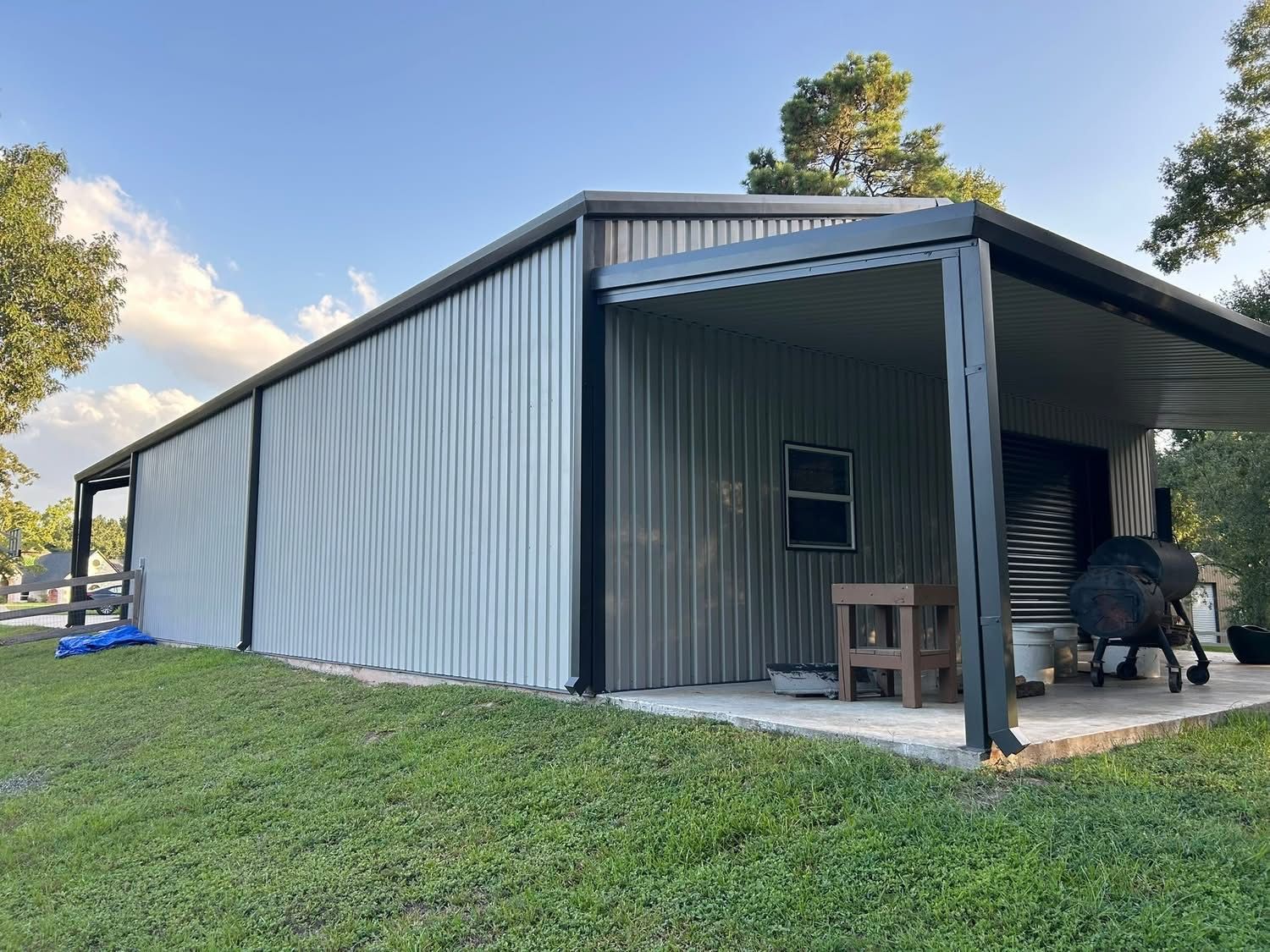 A metal building with a porch and gray corrugated walls, a black trim, and a concrete patio. New construction.