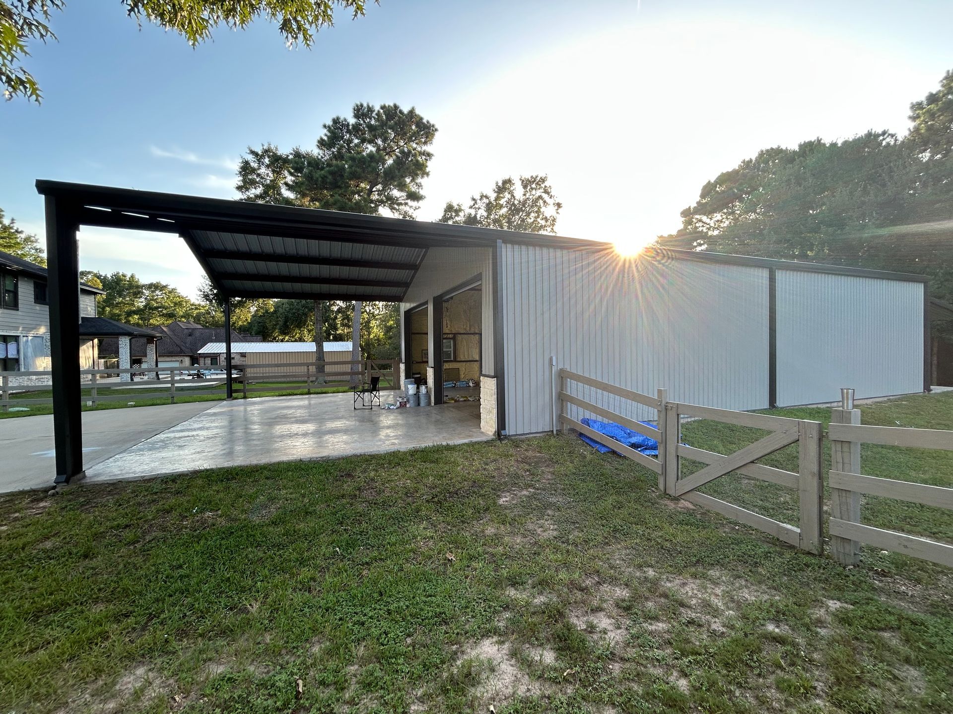 A metal workshop with a carport, a concrete pad, and a small fence. New construction.