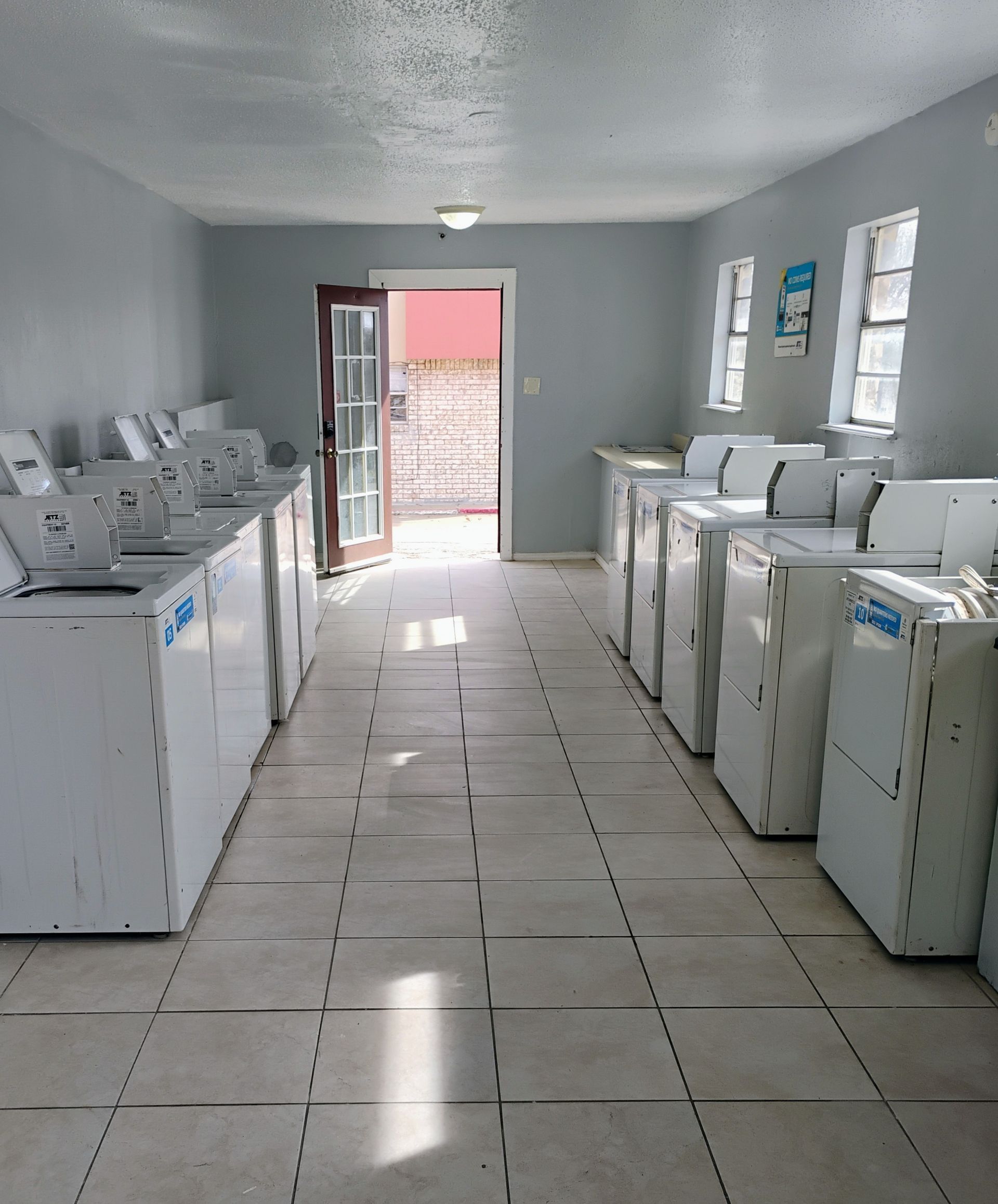 Laundry room with rows of white washing machines. Door open to outside.