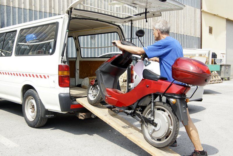 Un homme charge un scooter à l'arrière d'une camionnette