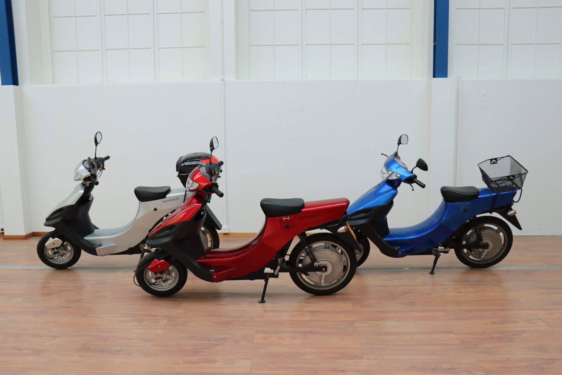 Trois scooters sont garés les uns à côté des autres sur un plancher en bois.