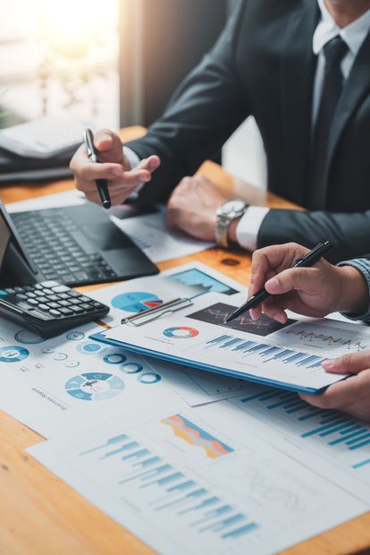 Due uomini d'affari esaminano i resoconti finanziari seduti a una scrivania con grafici e una calcolatrice.