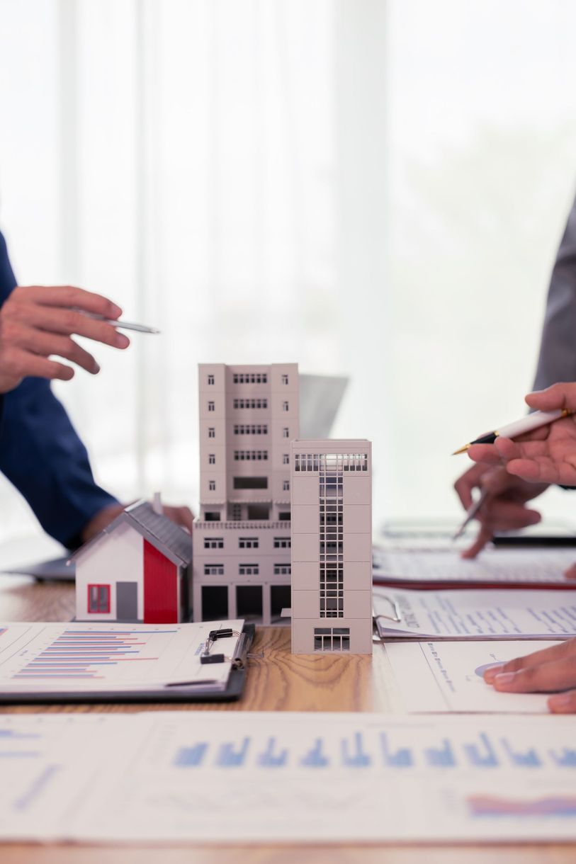 Persone che esaminano documenti, modelli di edifici su un tavolo, discutono progetti immobiliari.