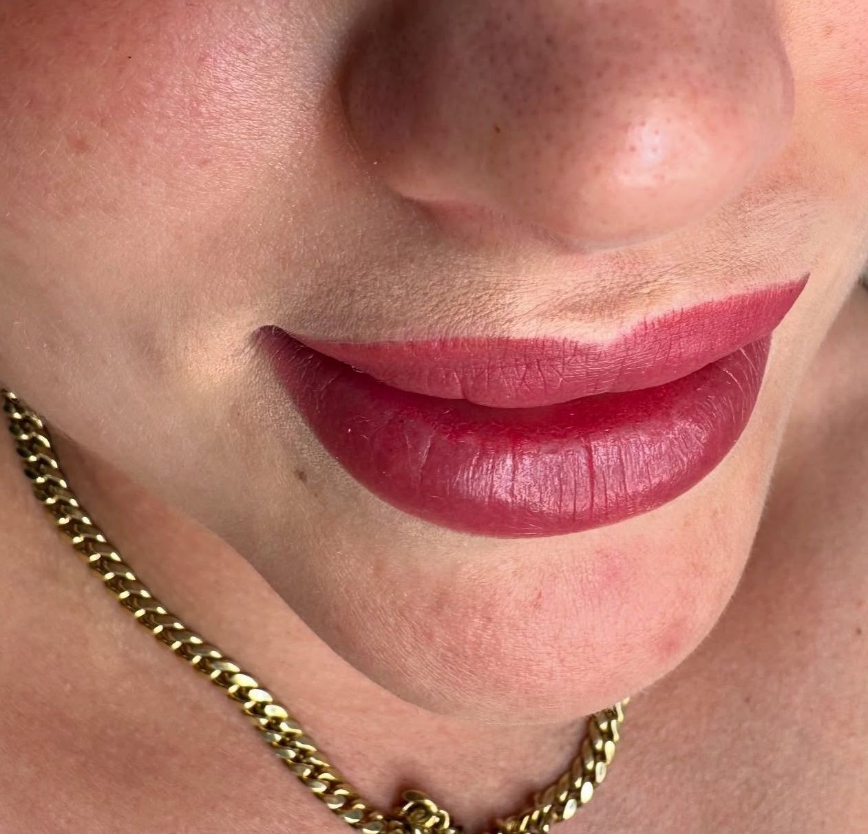 A close up of a woman 's lips with red lipstick and a gold chain around her neck.