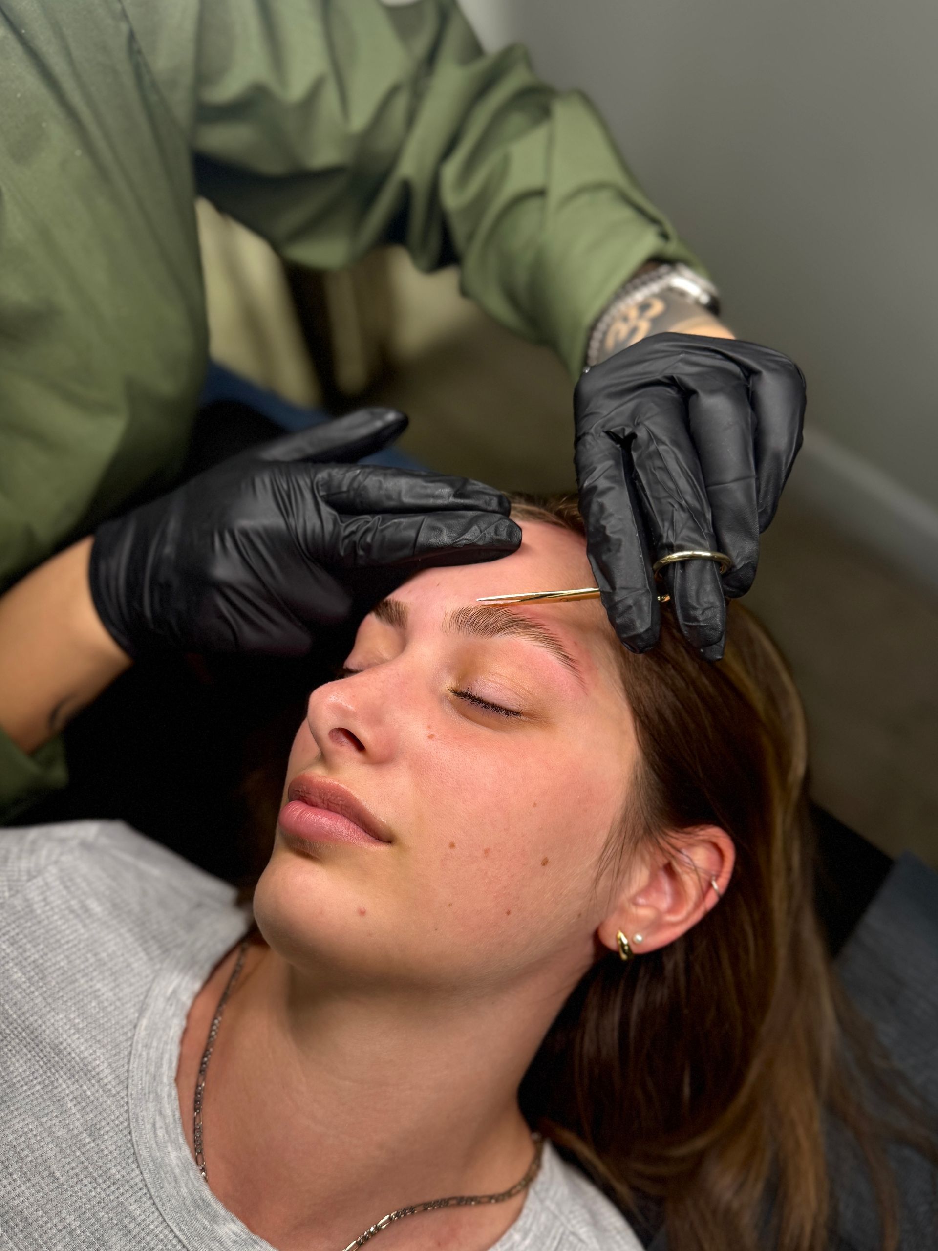 A woman is getting her eyebrows done by a man wearing black gloves.