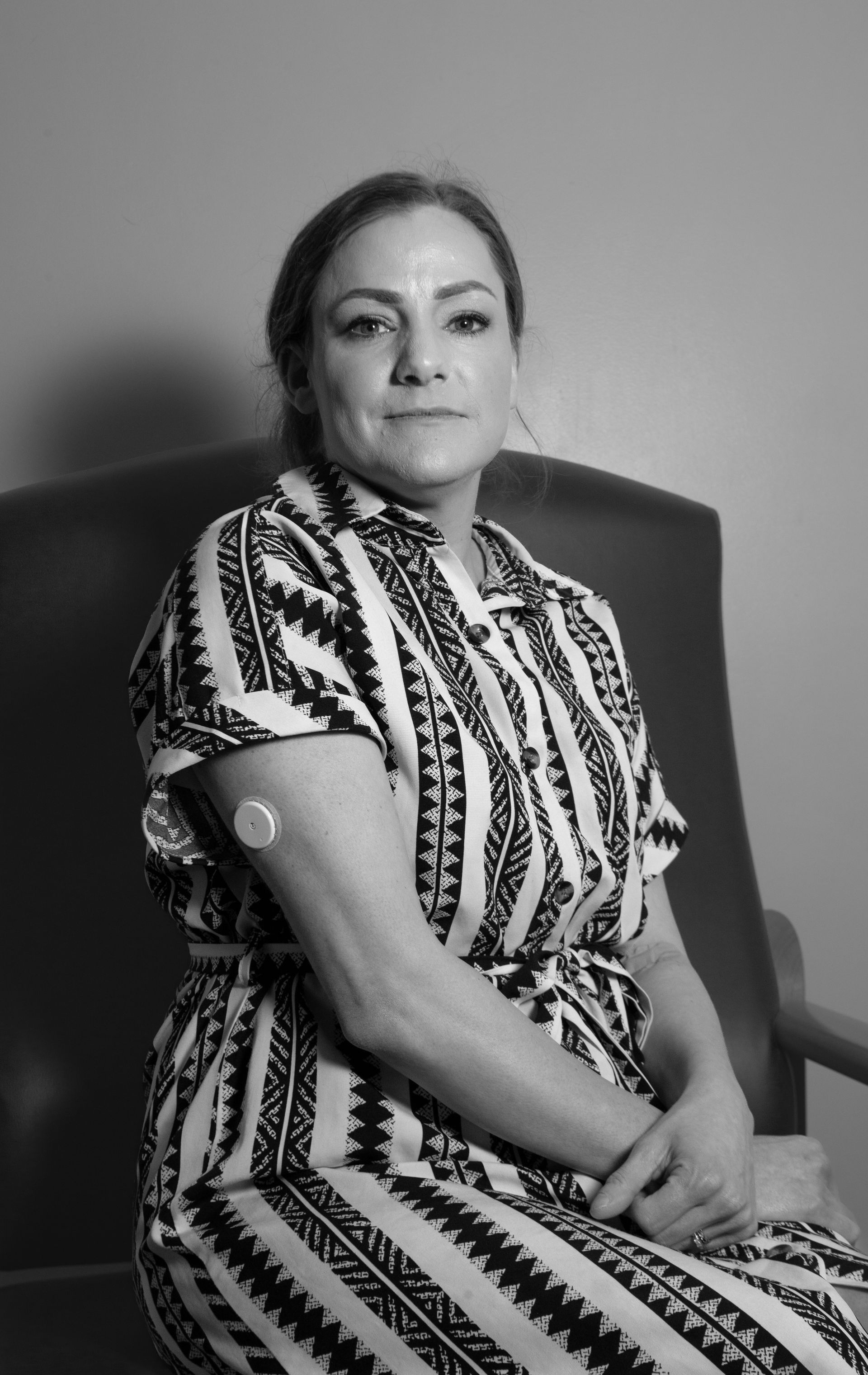 A woman is sitting in a chair with a patch on her arm.