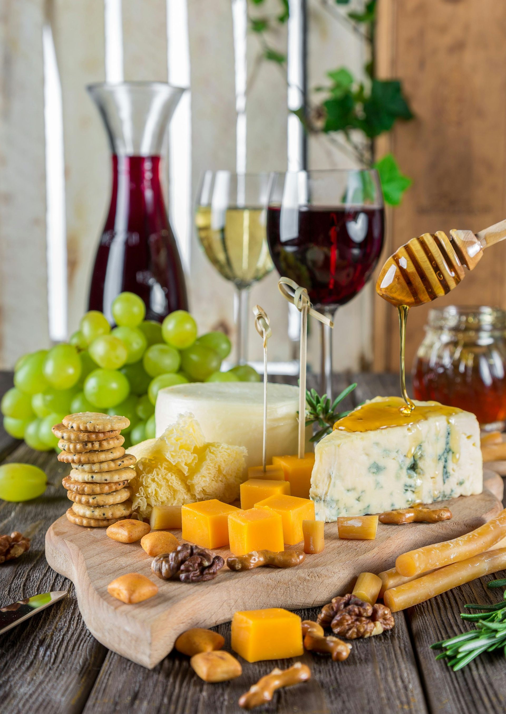 Cheese and crackers platter with grapes, wine glasses, nuts, and honey on a table