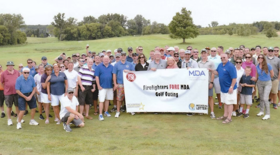 A large group poses on a golf course holding a banner for the Firefighters for MDA Golf Outing.