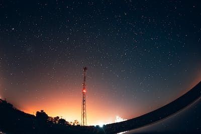 A telecommunication tower is silhouetted against a starry night sky.