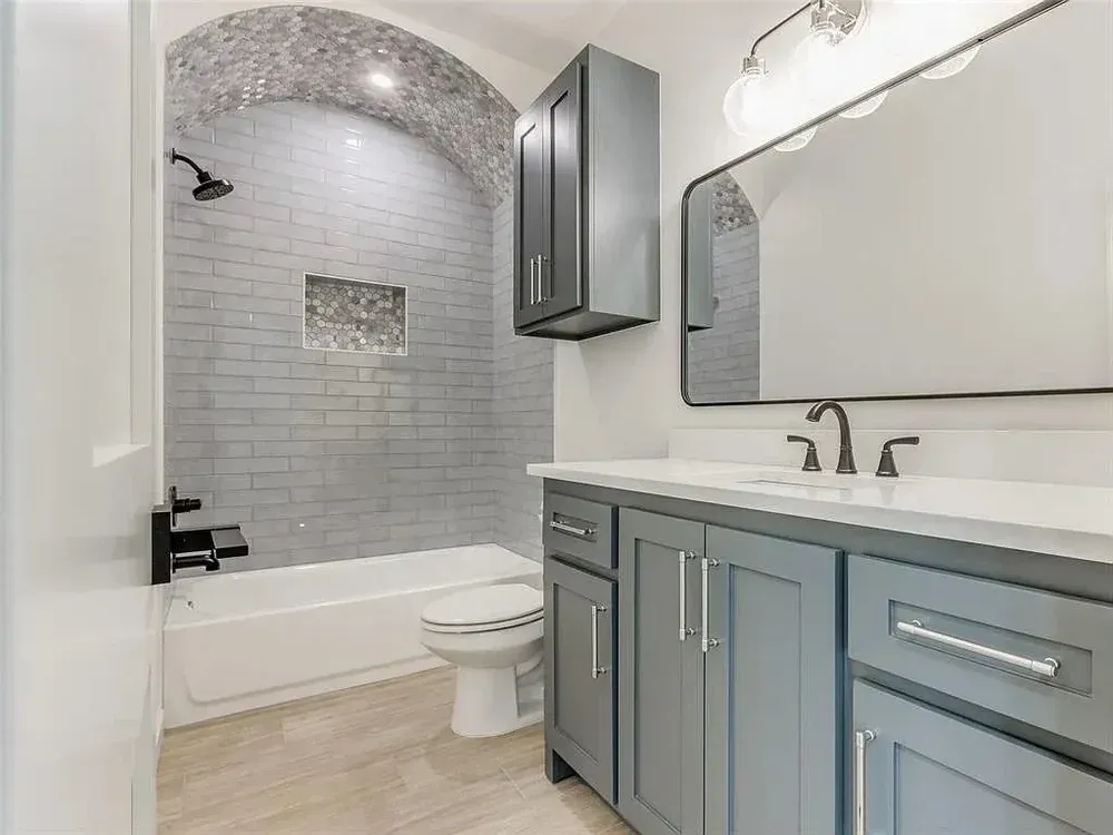 Bathroom with gray cabinets, white countertop, tile shower, and large mirror.
