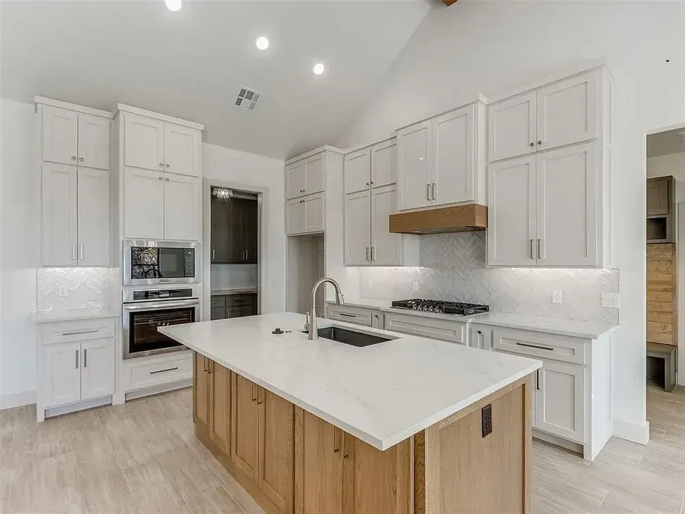 Modern kitchen with white cabinets, wood island, and light-colored tile flooring.