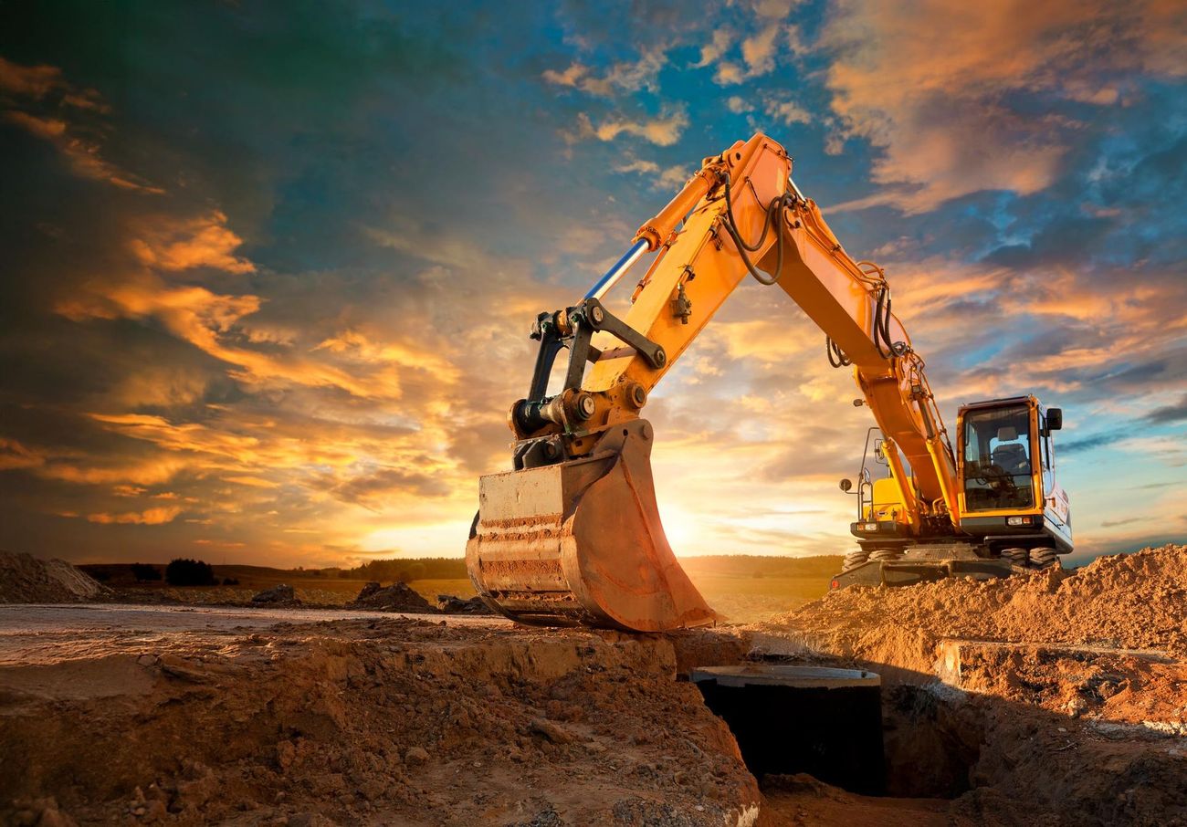 Yellow excavator digging in dirt, sunset sky.