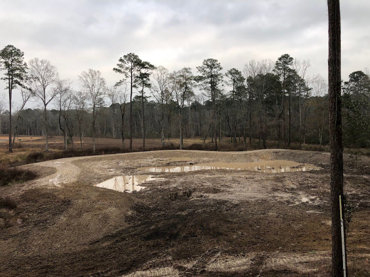 A tractor plows a field, separating green grass from brown soil under a cloudy sky.