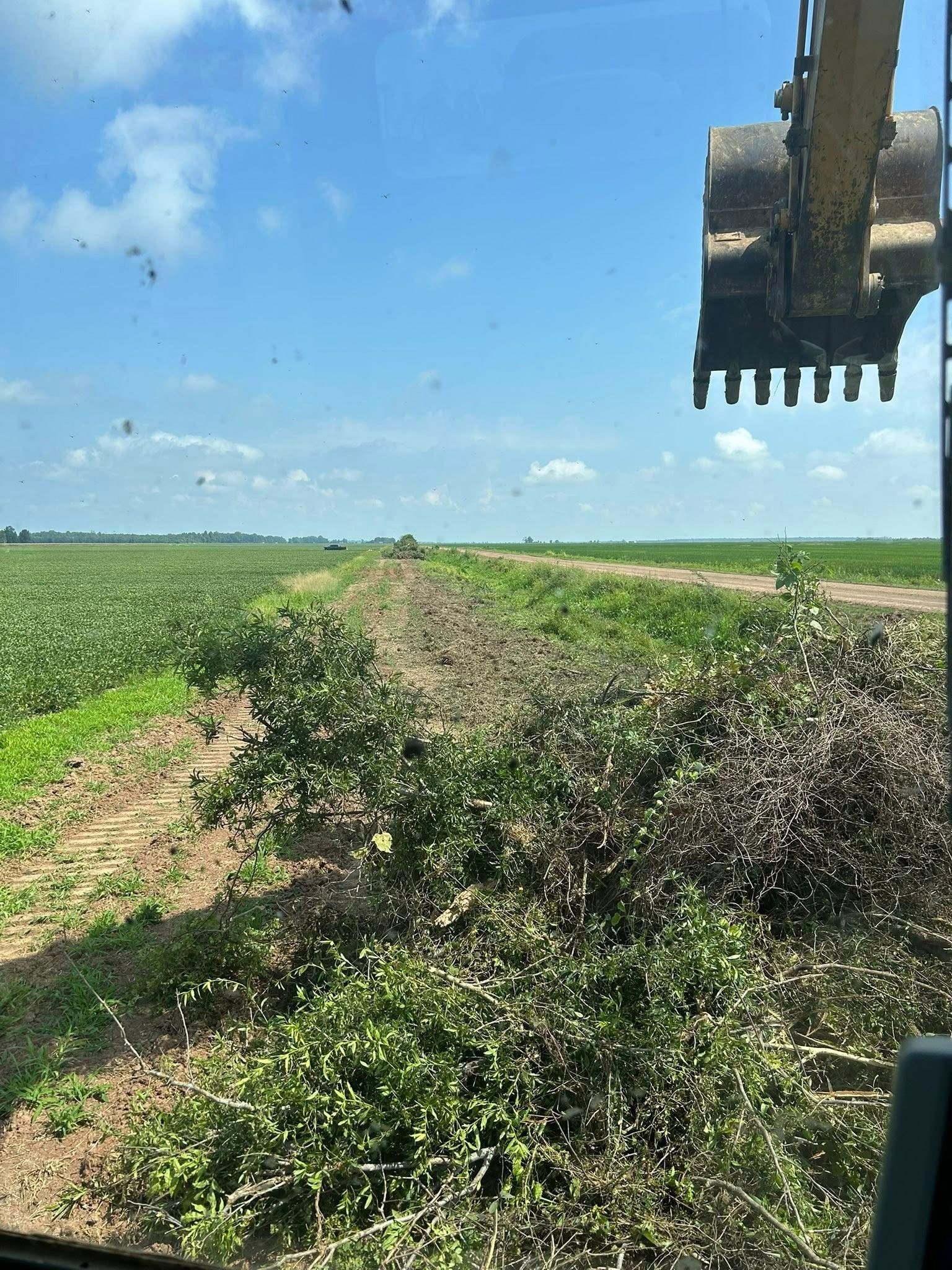 An excavator clearing brush along the edge of a field under a blue sky.