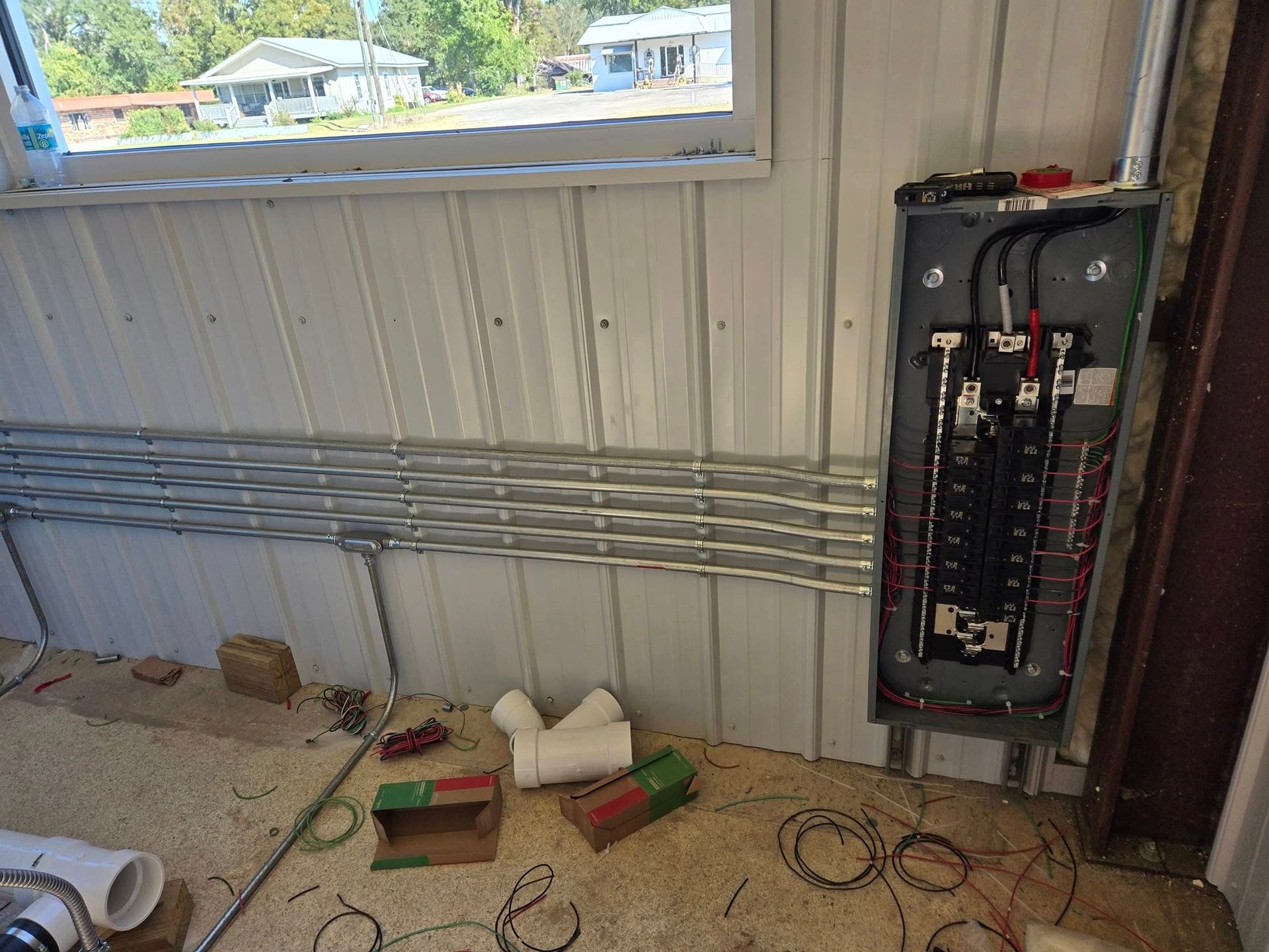 An electrical panel mounted on a corrugated metal wall with multiple conduits running horizontally to the left.