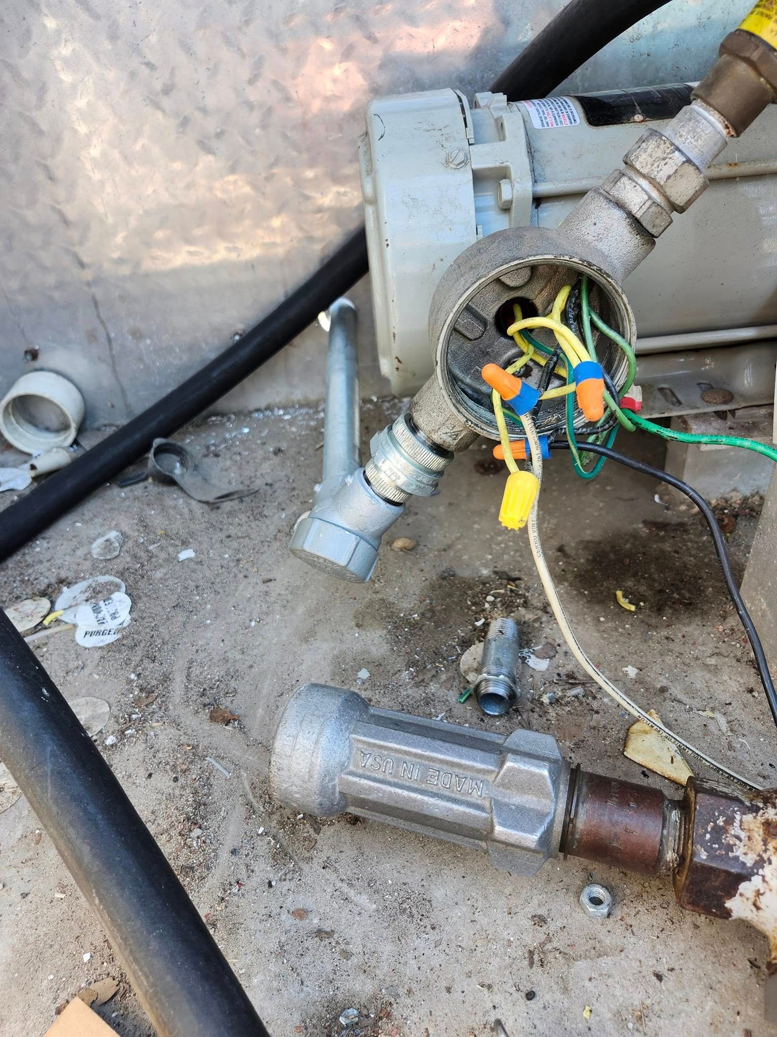 An open, exposed electrical junction box on a pump motor with various colored wires connected by plastic wire nuts.