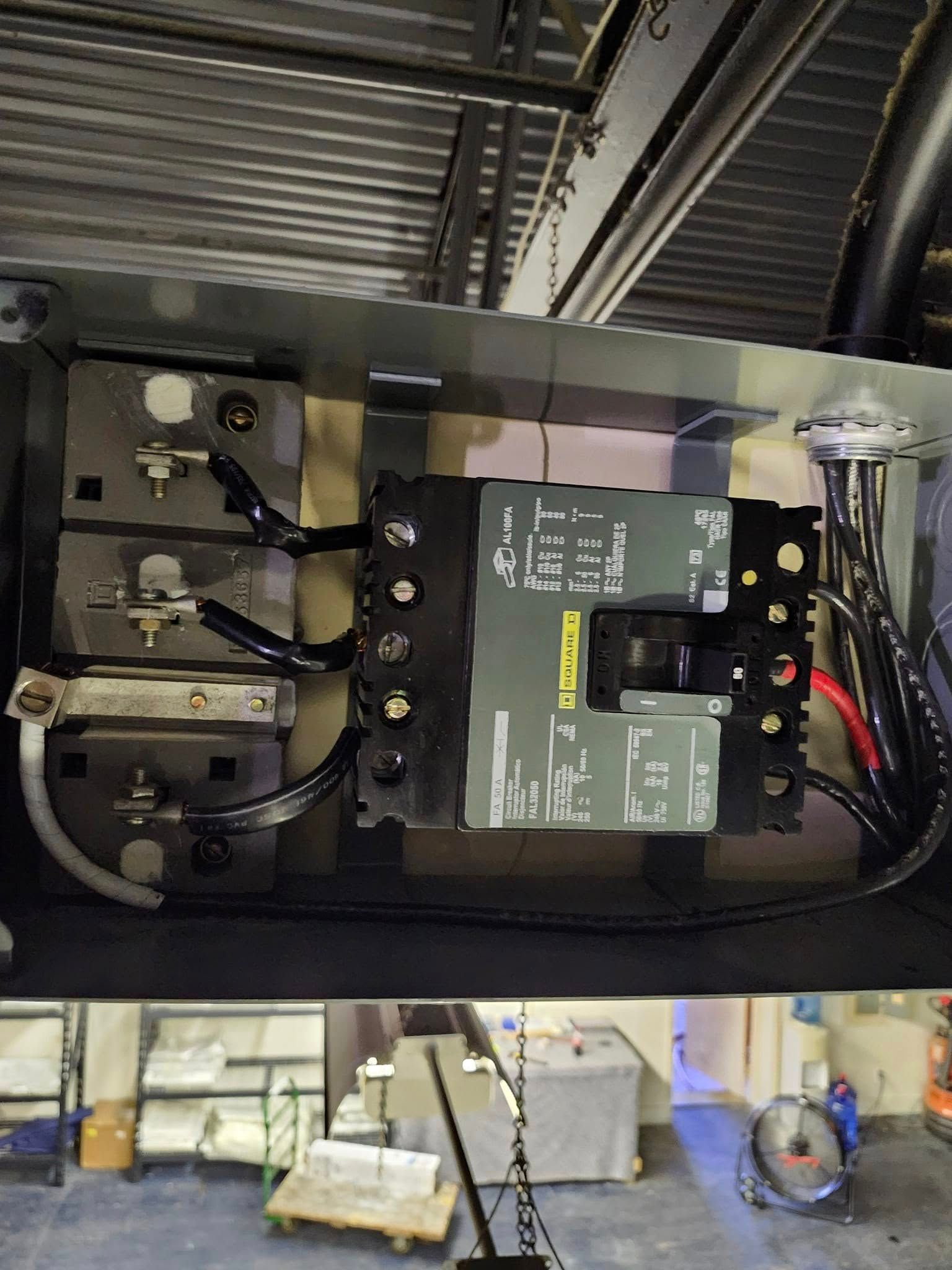 Open electrical junction box showing wiring connected to a black industrial circuit breaker and terminal blocks.