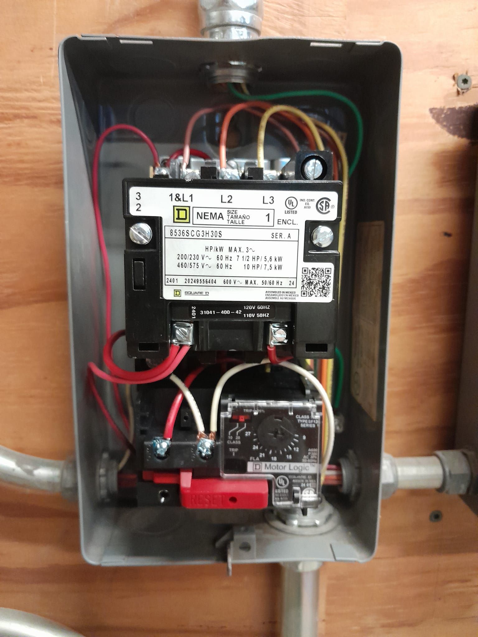 An open gray metal electrical box mounted on plywood containing a Square D magnetic motor starter with wiring connections.