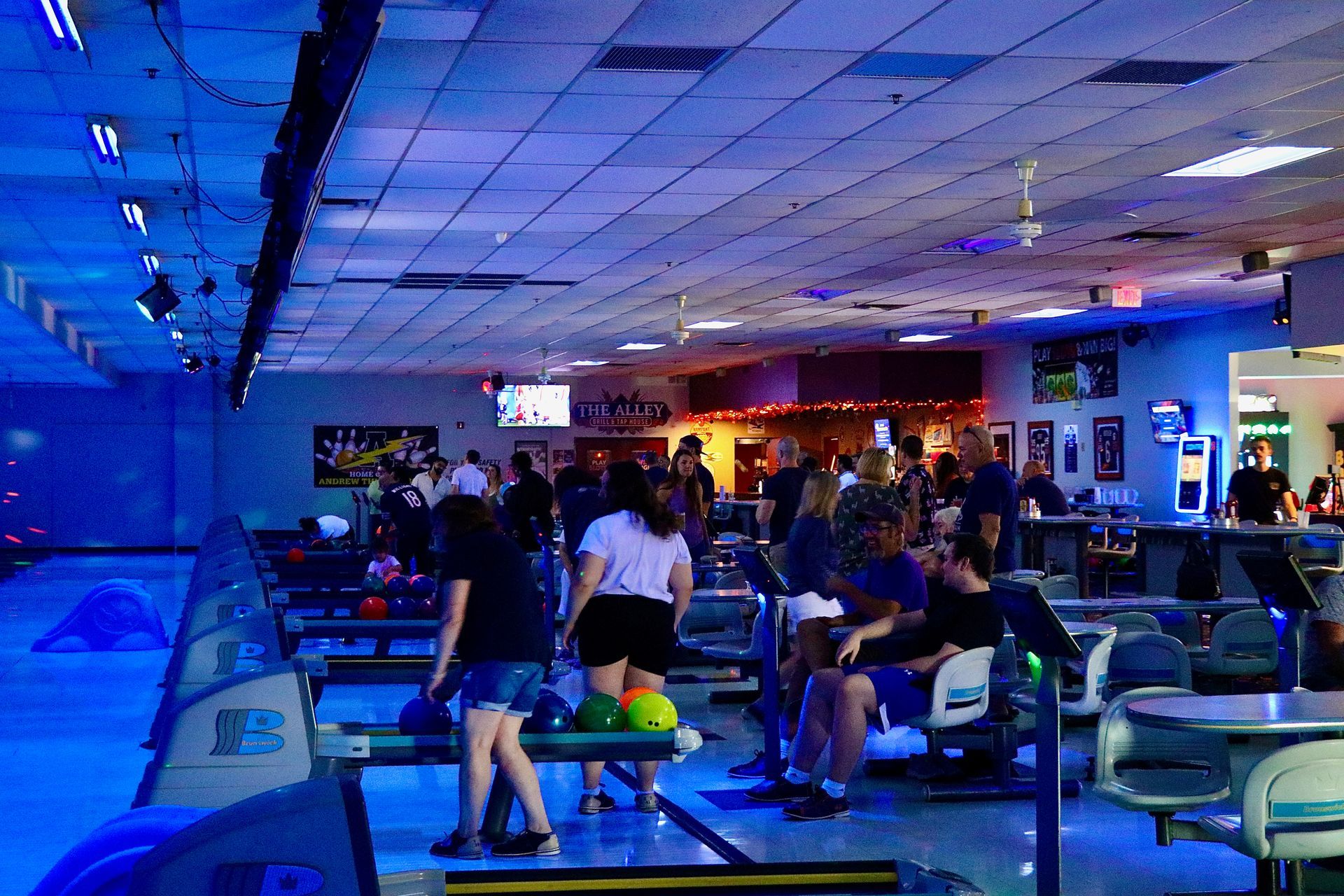 Bowling alley interior with people, blue neon lighting, and bowling lanes.
