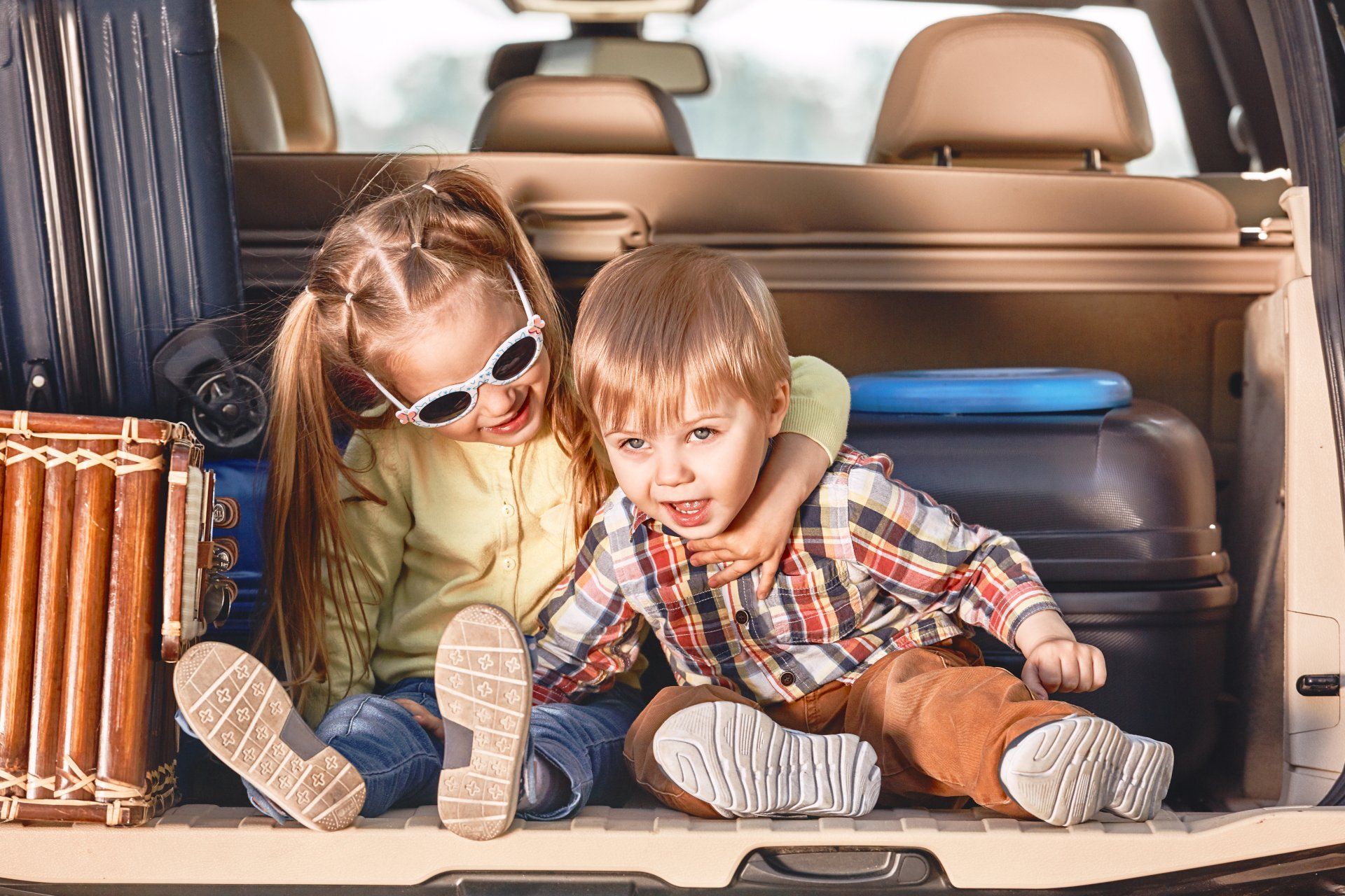 Um menino e uma menina estão sentados na traseira de um carro com bagagem.