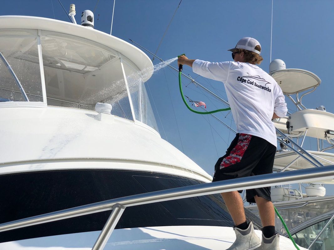 Man in white shirt washes a white yacht on a sunny day.