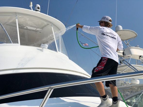 Person spraying water on a white yacht on a sunny day.