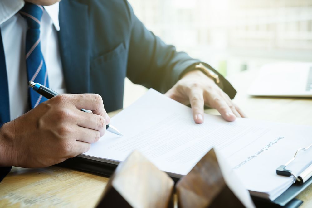 A Man in a Suit and Tie is Writing on a Piece of Paper — Karlene's Conveyancing In Avoca, NSW