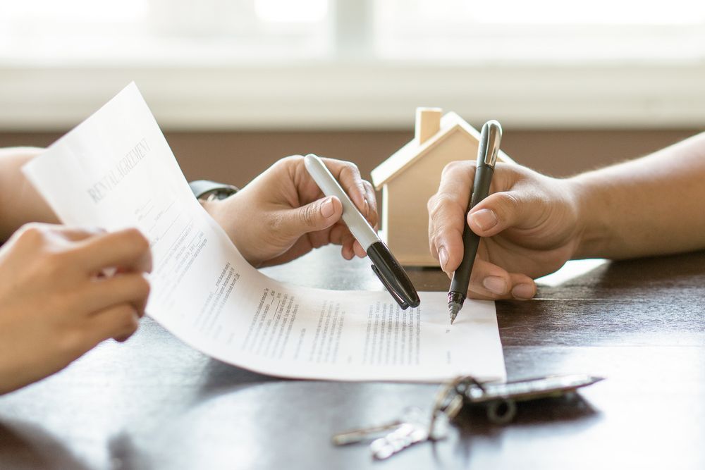 A Couple of People Are Sitting at a Table Signing a Contract — Karlene's Conveyancing In Avoca, NSW