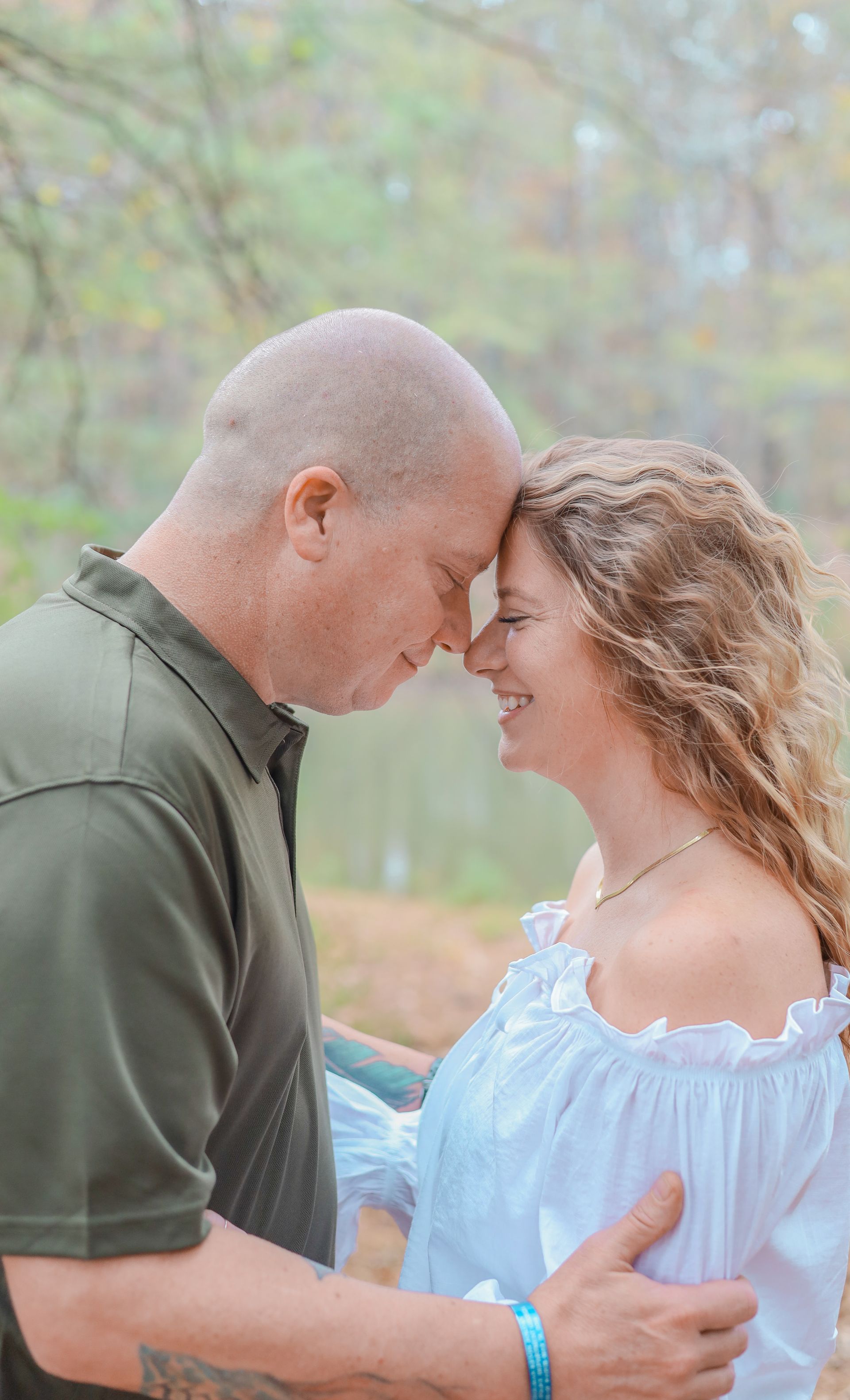 Couple touching foreheads, smiling, outdoors near water. Man in green shirt, woman in white.