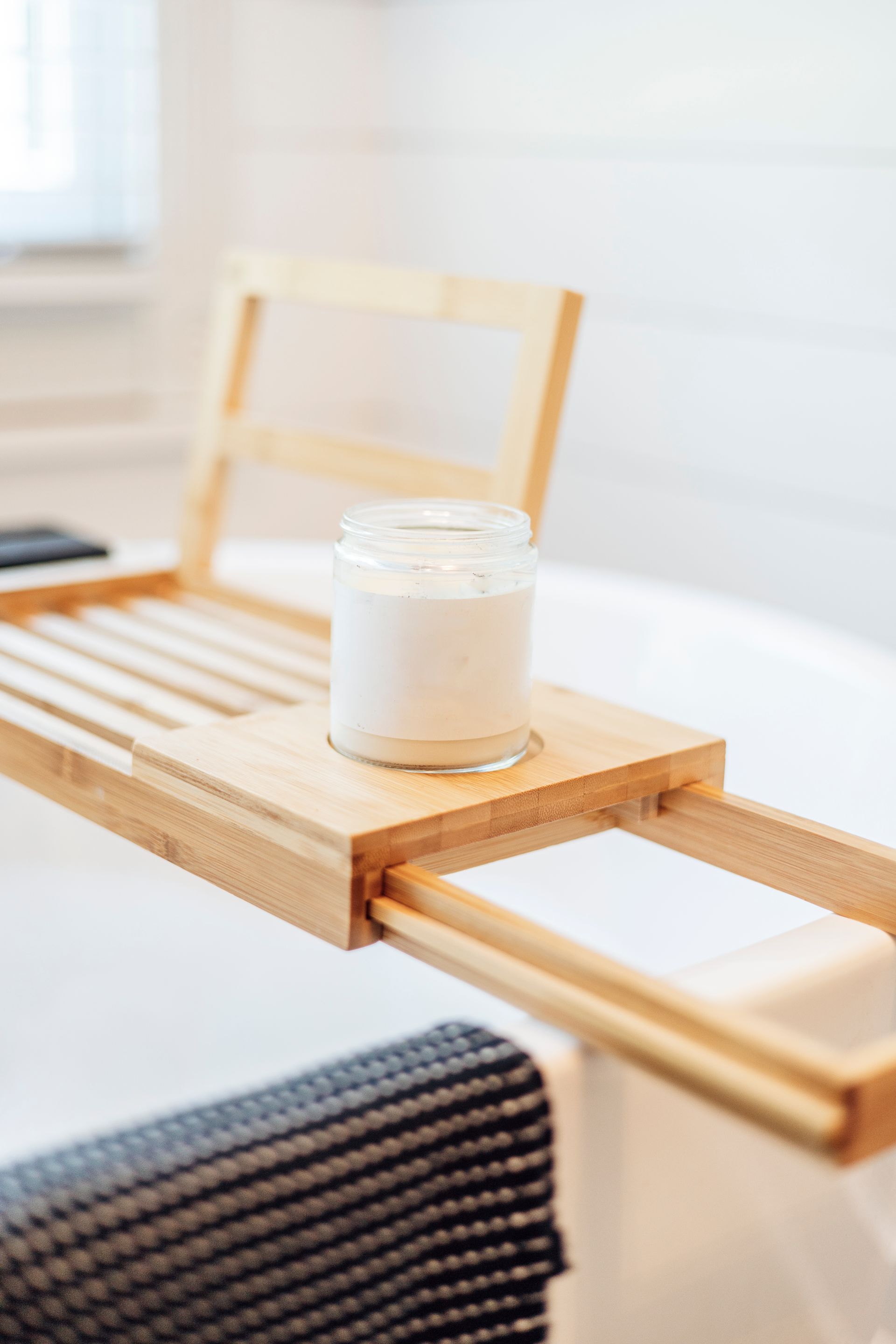 Wooden bath tray with a jar on a white bathtub, a towel is draped on the side.