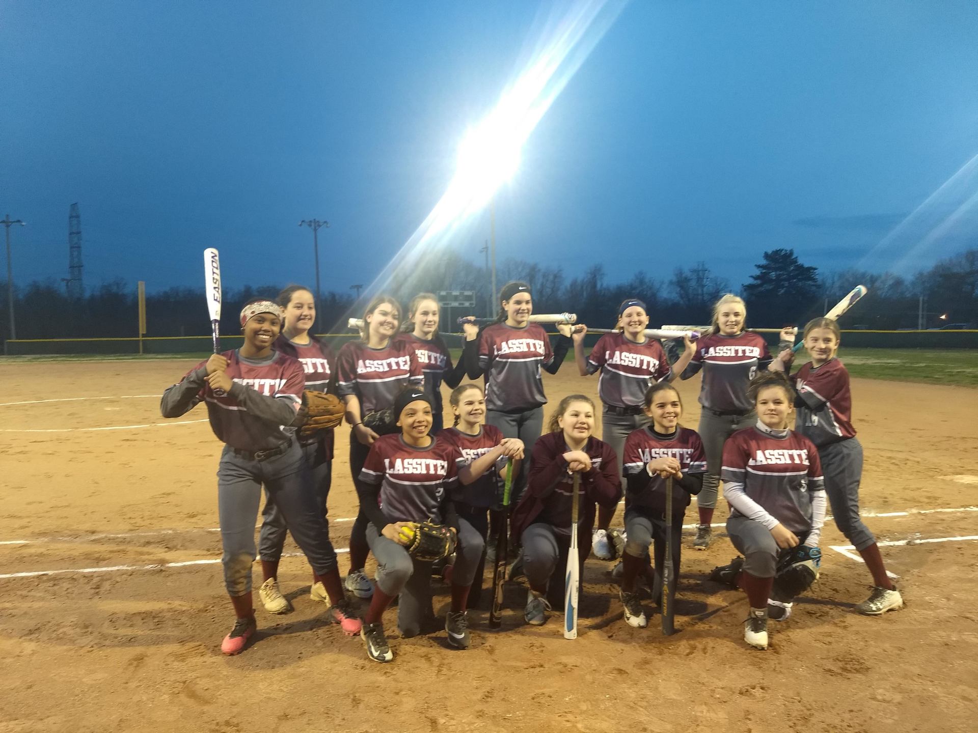 a group of softball players are posing for a picture on a field .