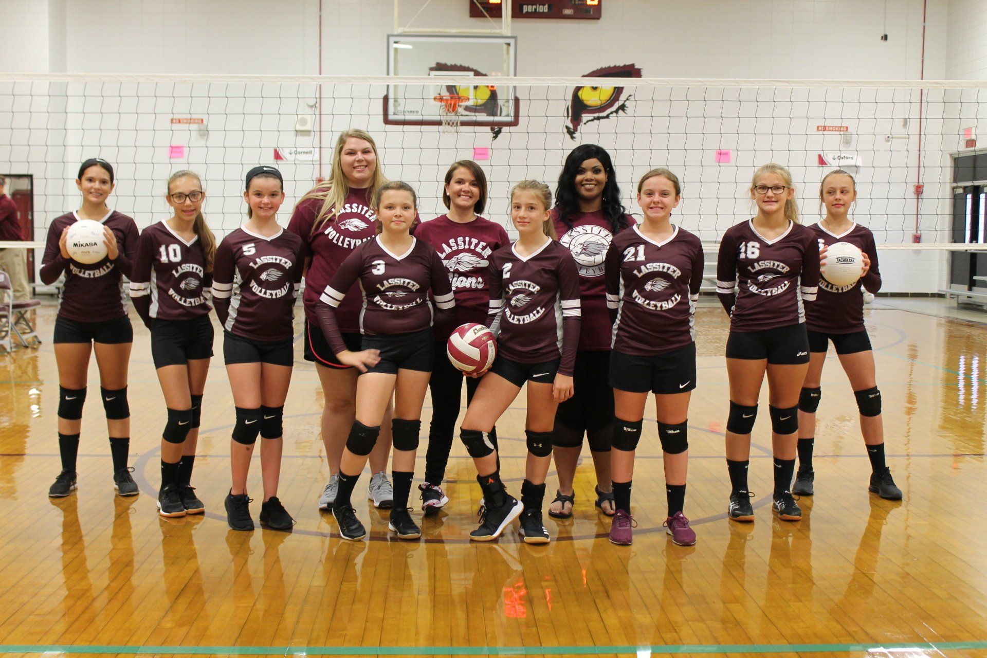 a group of girls are posing for a picture in front of a volleyball net .