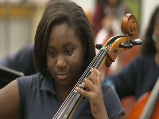 a young girl is playing a cello in an orchestra .