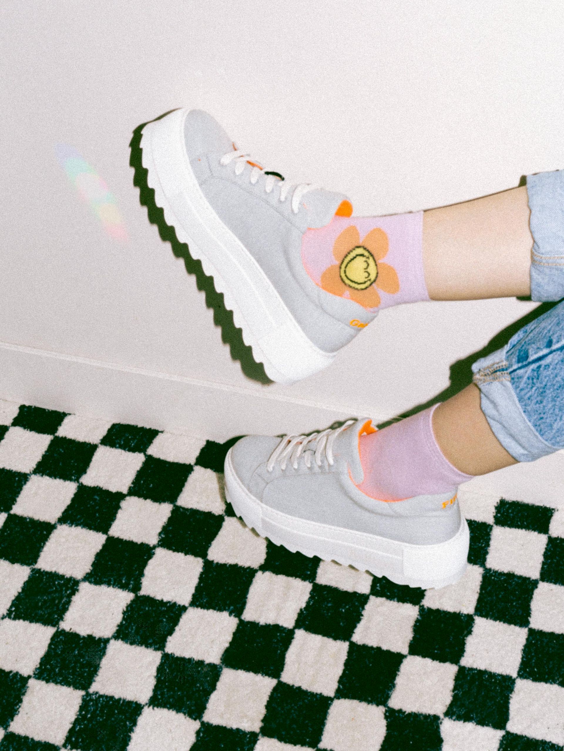Feet with grey sneakers and flower-print socks on a checkered floor.