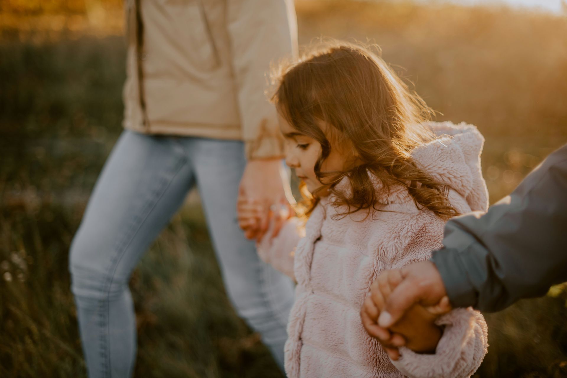 Parents smile at a toddler, who is being held. The family is outside near water.
