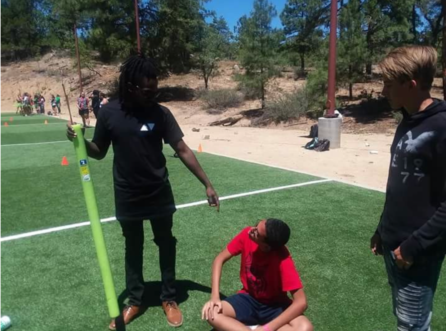 A man is holding a green stick while a boy sits on the grass