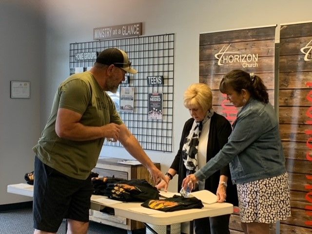 A man and two women are standing around a table.