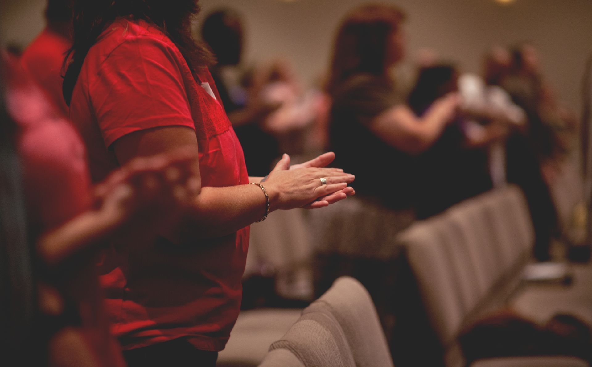 A woman in a red shirt is clapping her hands in a church.