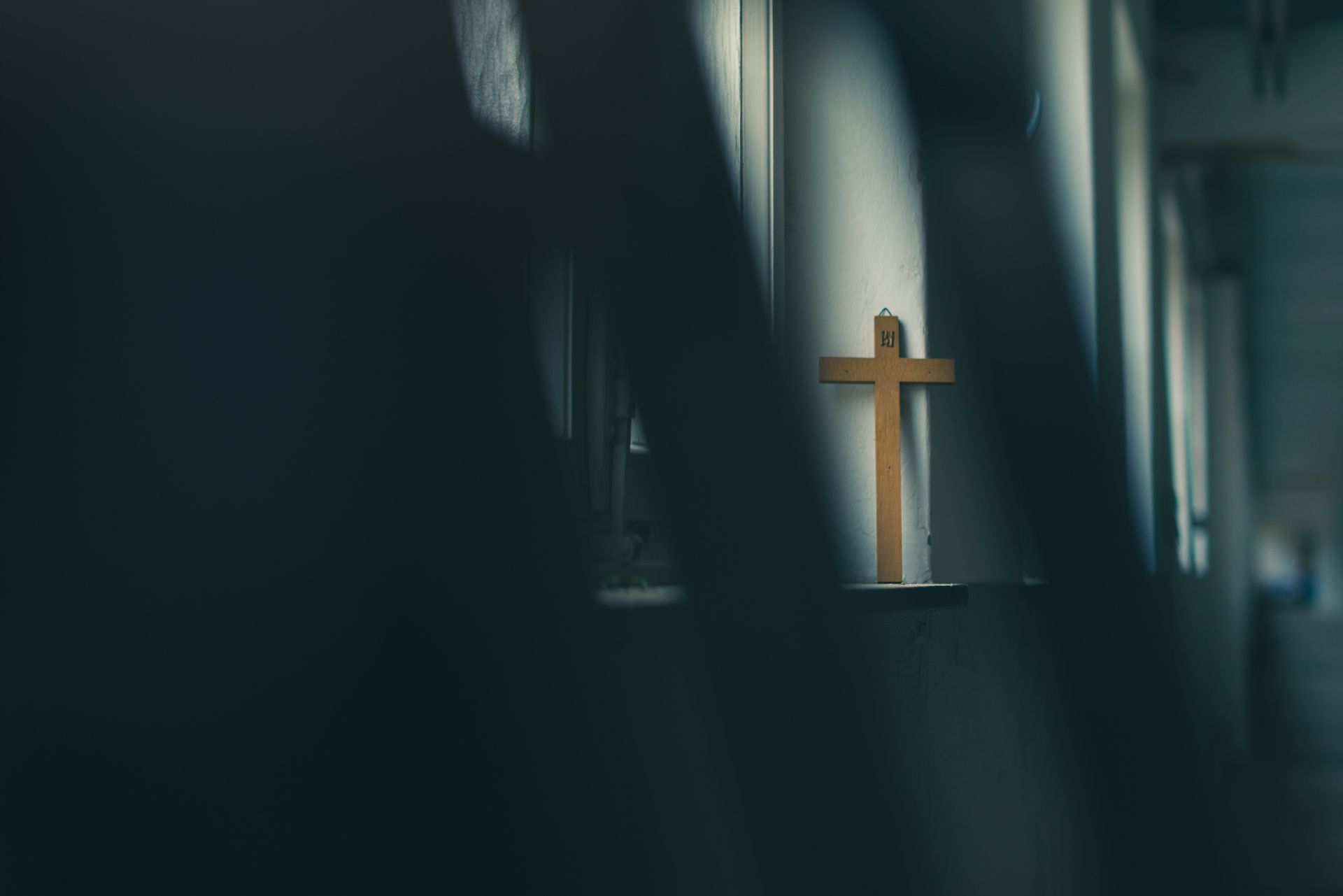 A wooden cross is hanging on a wall in a dark church.
