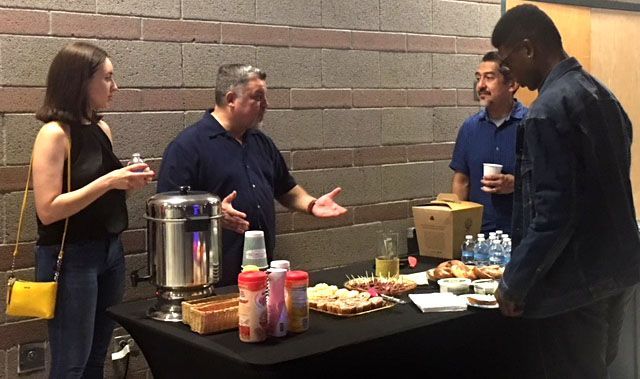 A group of people are standing around a table with food on it.